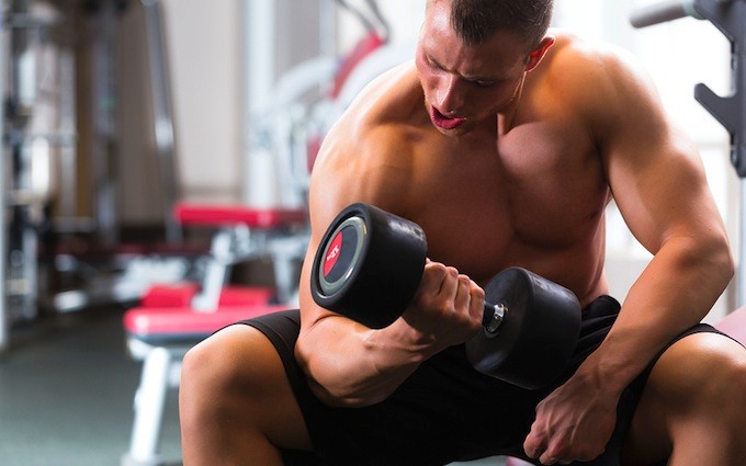 Strong man, bodybuilder exercising with dumbbells in a gym